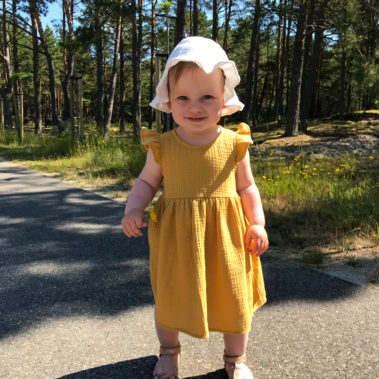 mała dziewczynka w żółtej muślinowej sukience stojąca wśród drzew