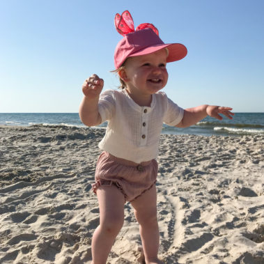dziewczynka na plaży ubrana w muślinowe spodenki w kolorze brudnego różu